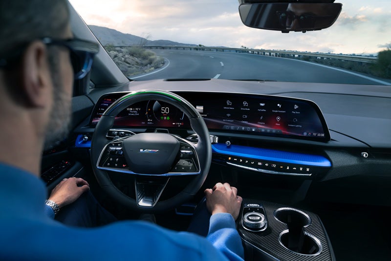 Front View of the 2026 OPTIQ-V Driving Through the Dusk Utilizing its Headlights | Prestige Cadillac in WARREN MI