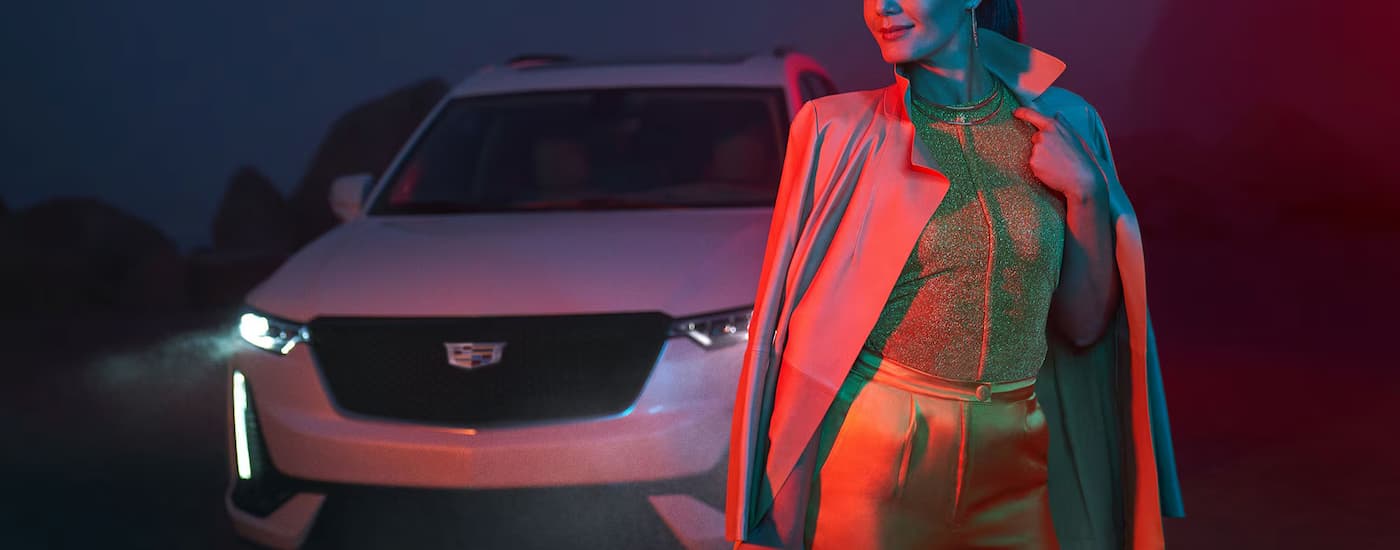 A woman illuminated in red light is walking away from a white 2025 Cadillac XT5.