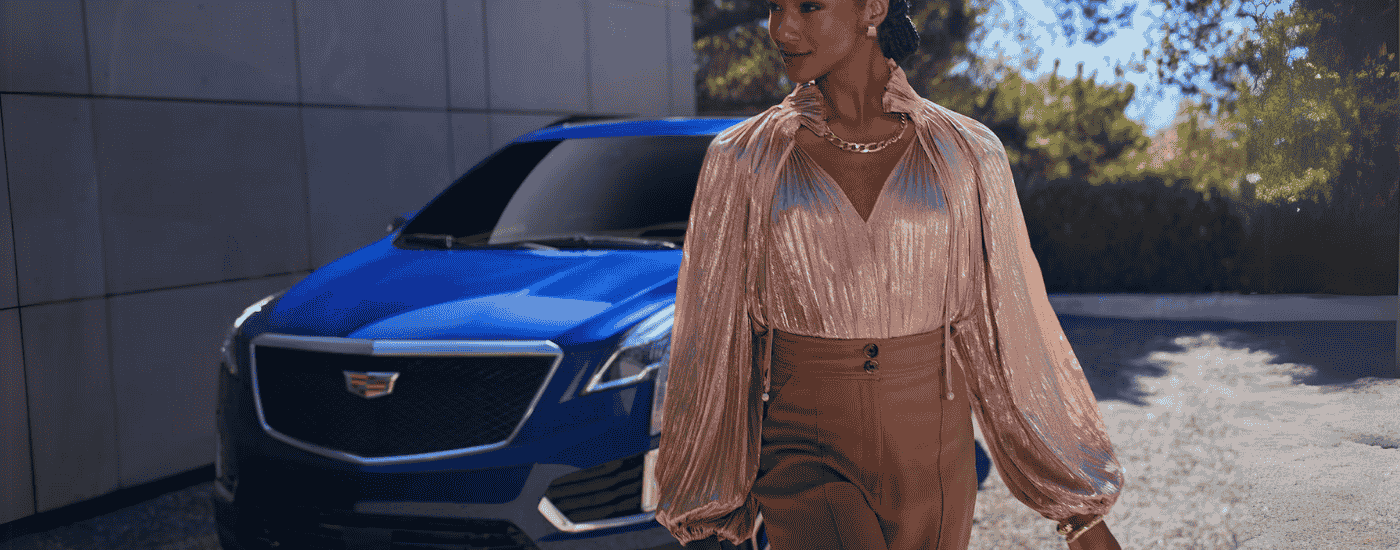 Woman walking past a blue 2025 Cadillac XT5 at a Cadillac dealer near Sterling Heights.