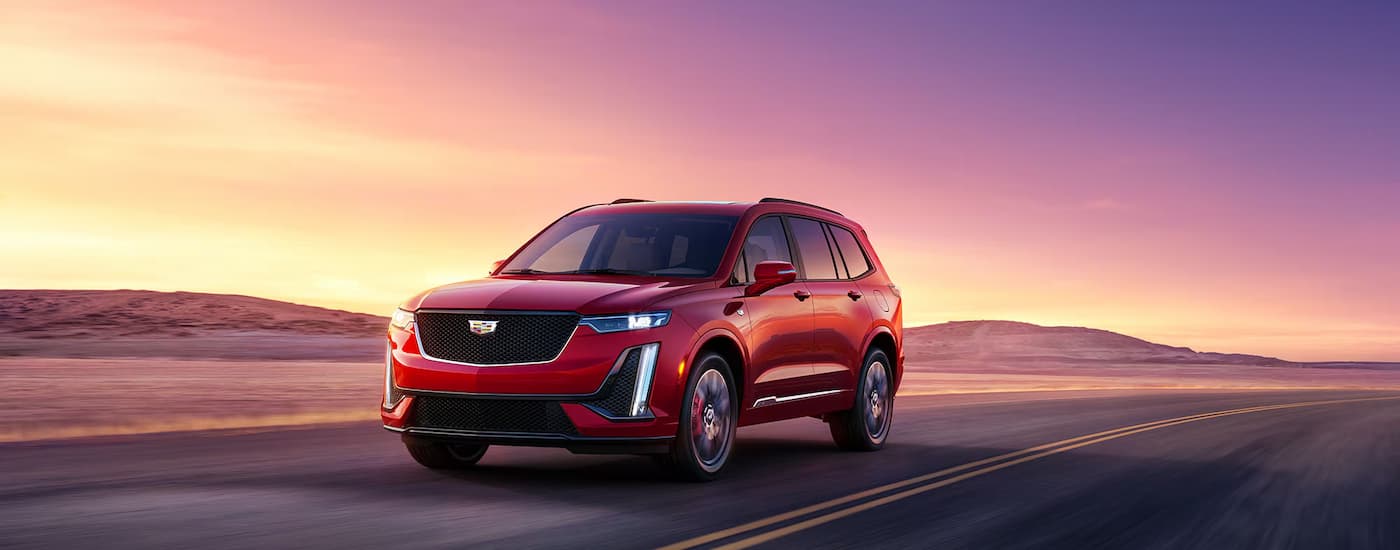 A red 2025 Cadillac XT6 driving down a road at sunset