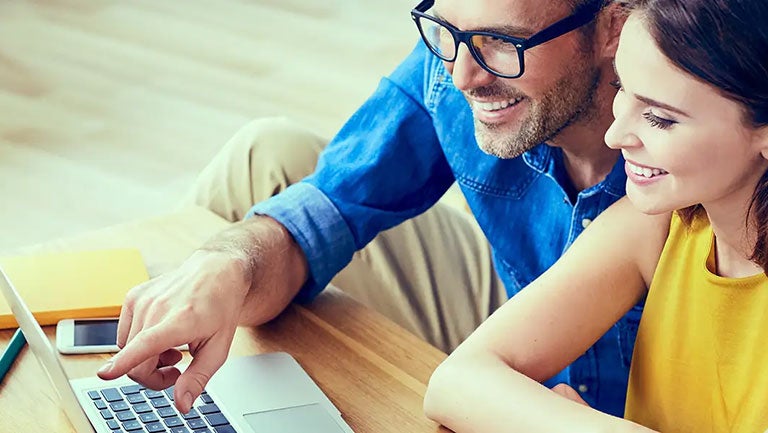 A man and woman smiling while looking at a laptop