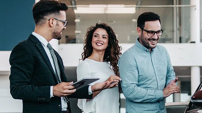 A man and woman looking at a vehicle and speaking with a salesman