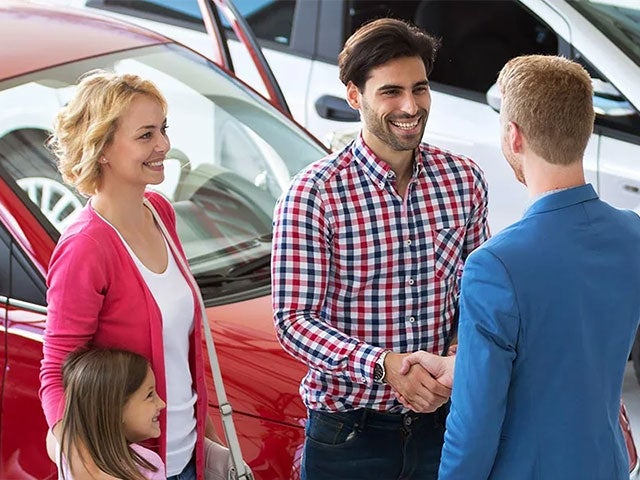 A family of three smiling and shaking hands with a salesman in the showroom