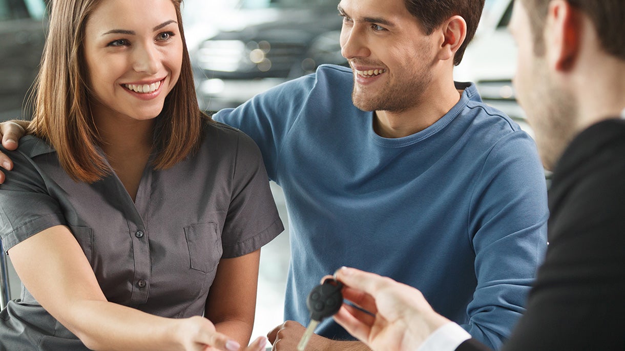 A man and woman receiving car keys from a salesman